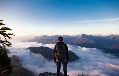 man in black jacket and black pants standing on rock formation looking at mountains
